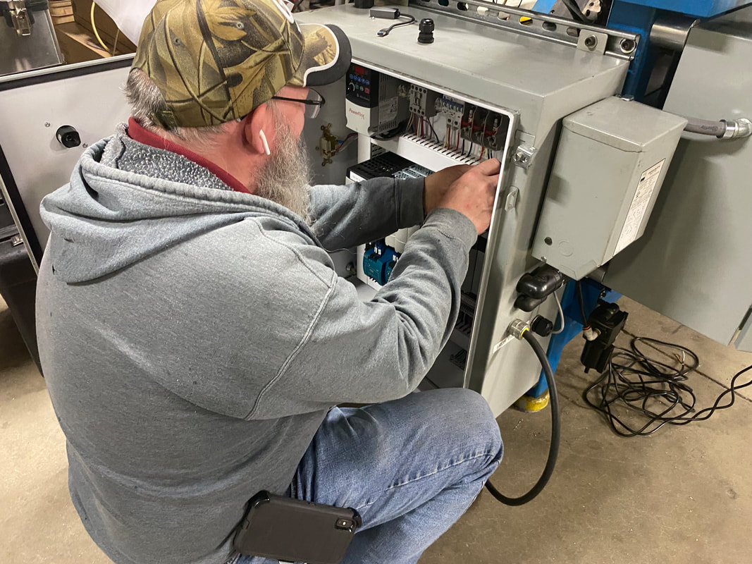 An automation technician working on the electrical panel of a machine.